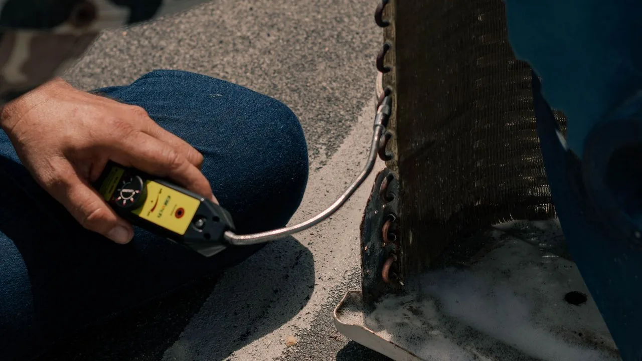 A technician testing an outdoor air conditioning condenser coil with a handheld meter.