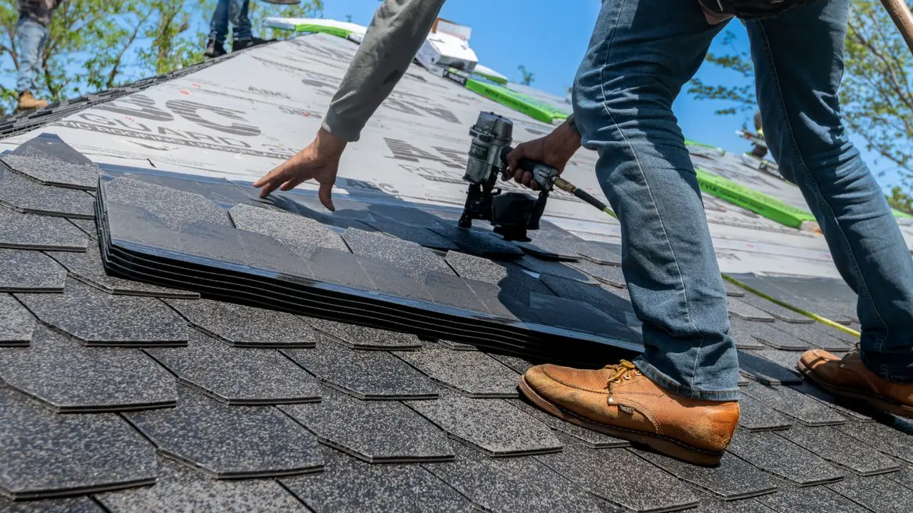 A roofer fixing a course of architectural asphalt shingles with a coil nail gun.